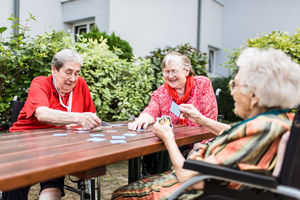 Drei ältere Menschen spielen zusammen Karten am Tisch im Freien.